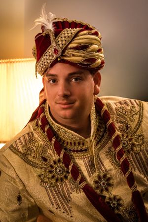 Close-up portrait of groom in cream and gold sherwani with red turban.