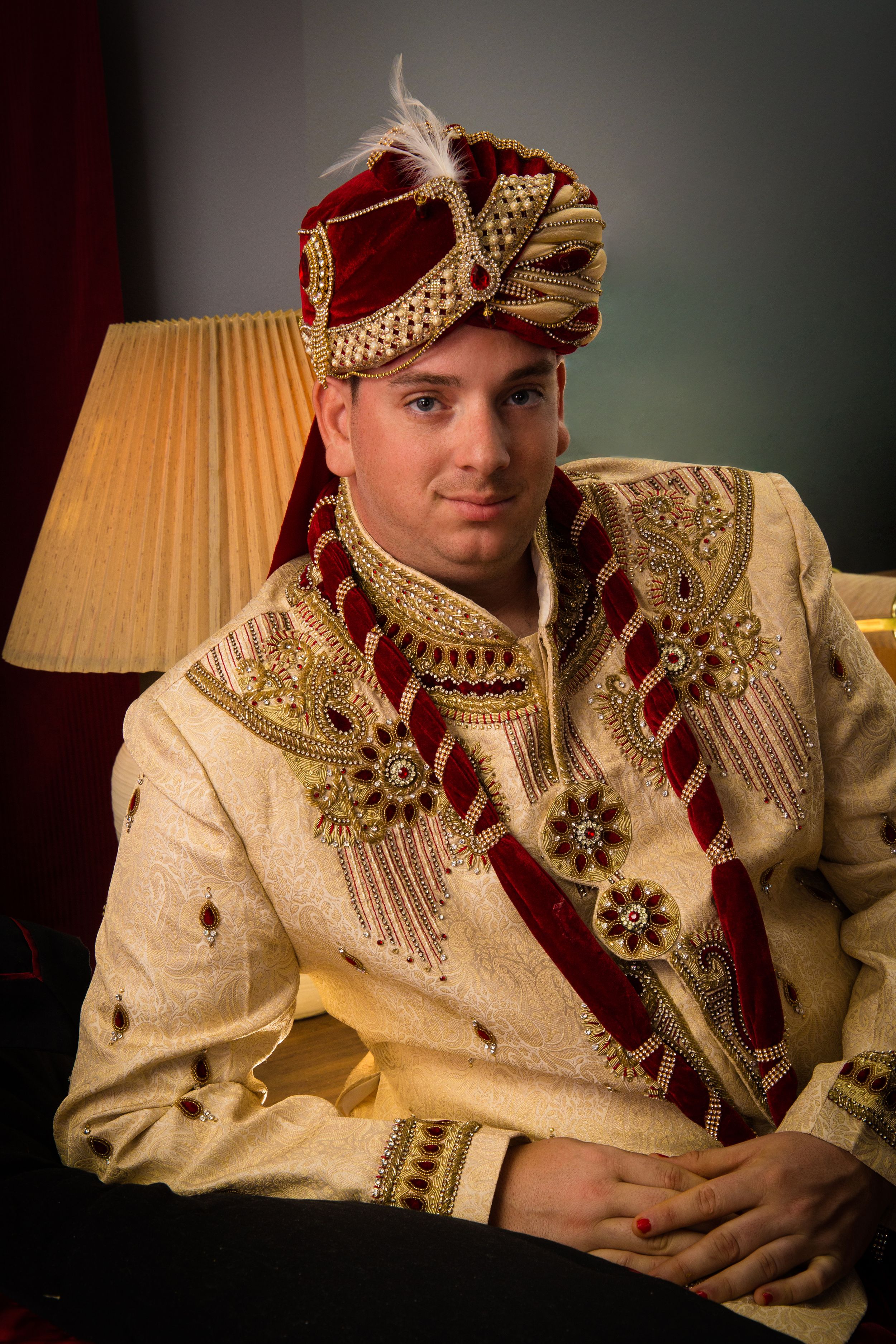 Groom in traditional Indian wedding outfit posing against dark background.