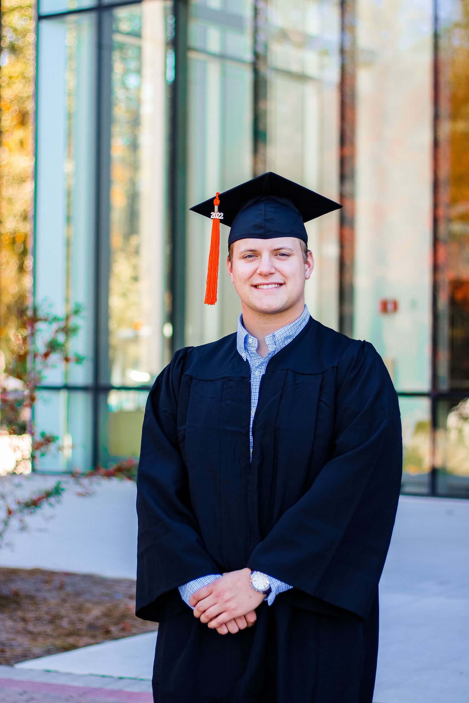 Graduate in traditional black cap and gown smiles in front of modern building on graduation day.
