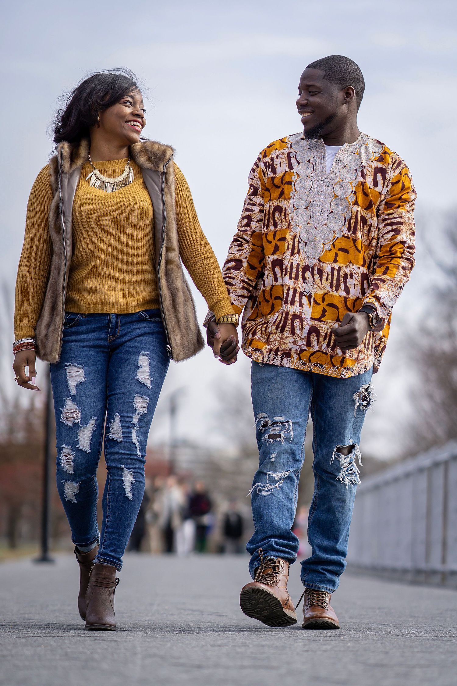 A couple in matching yellow and brown outfits walk hand in hand along a bridge pathway.