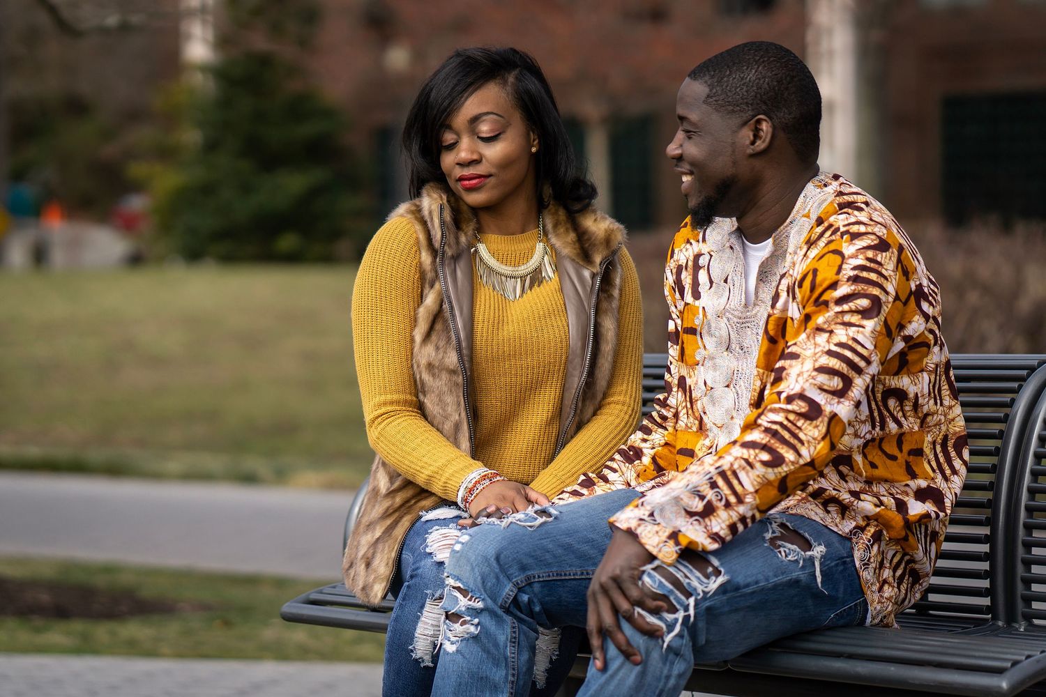 A couple in casual attire having a conversation while relaxing on an outdoor bench.