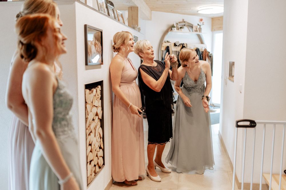 A group of women in formal dresses gather in a hallway during wedding preparations.