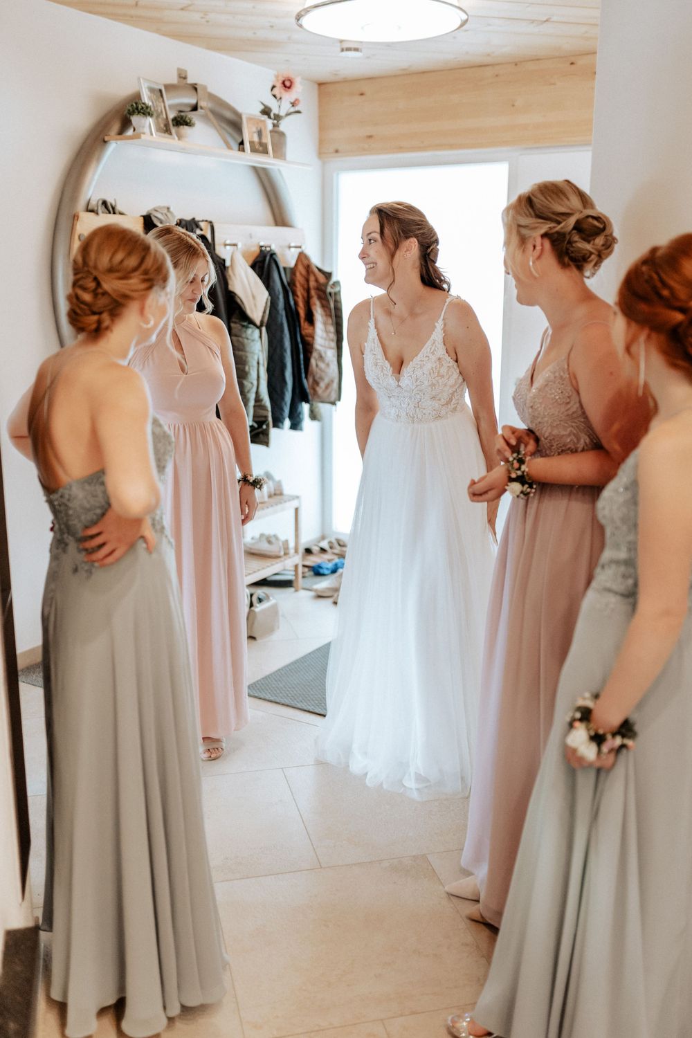 Bridesmaids in pastel dresses admiring the bride in her white gown during wedding preparations.