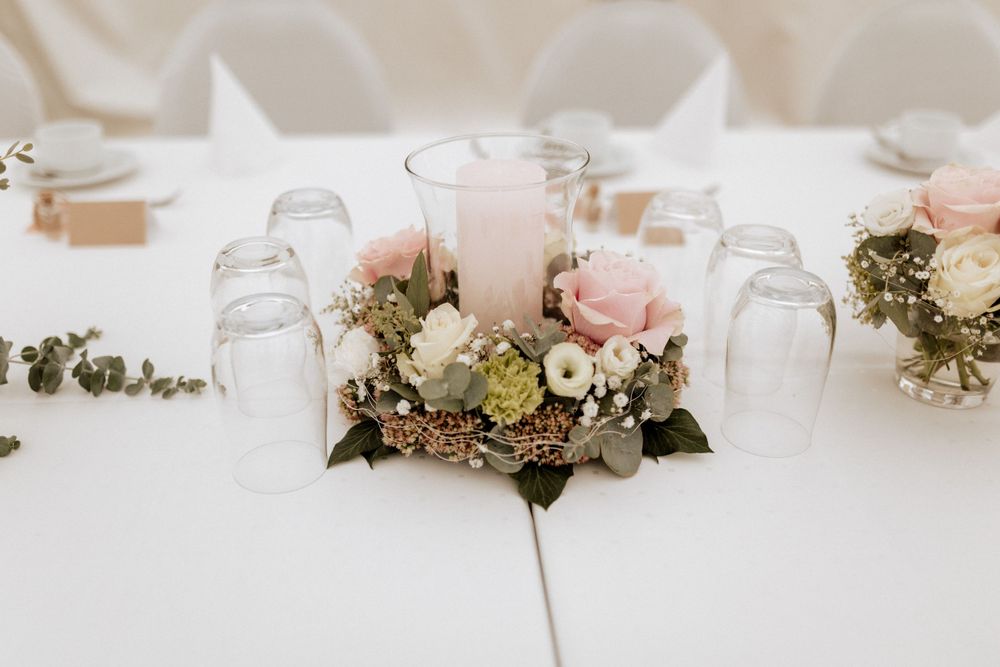 A romantic centerpiece with pink roses and greenery surrounding a white candle on a reception table.