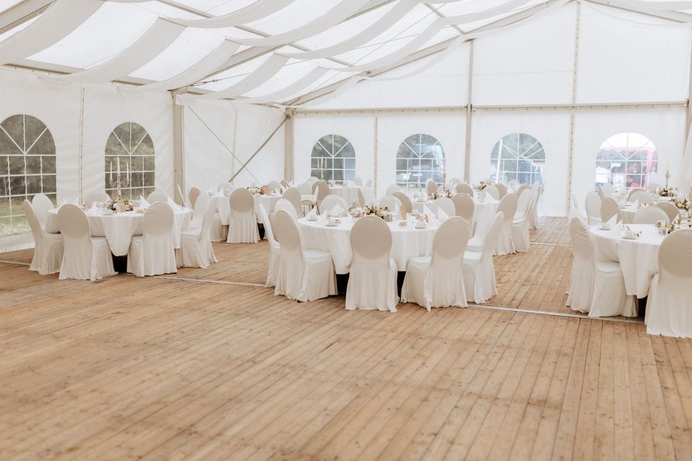 An elegant white wedding reception tent with covered chairs and tables set for dining.