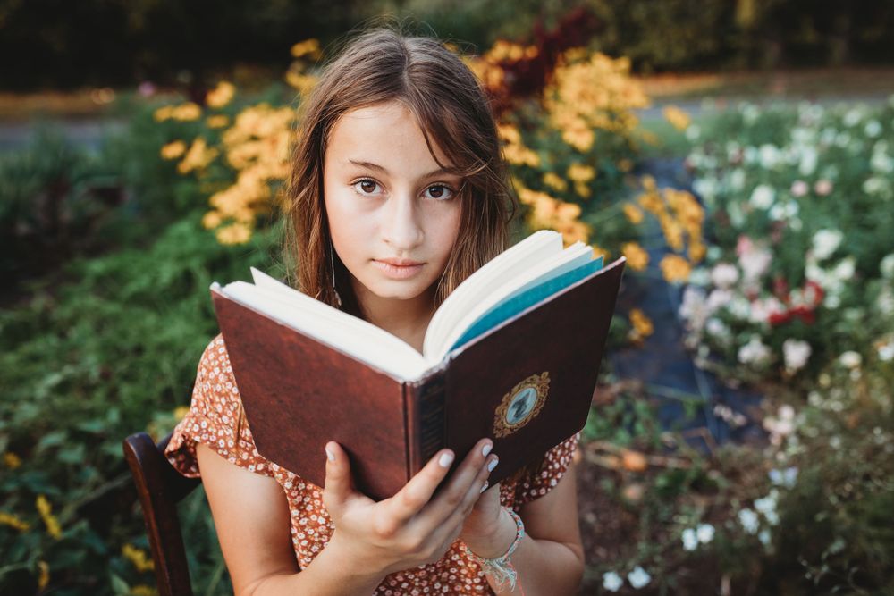 Someone holding an open book while sitting in a colorful garden with yellow flowers.
