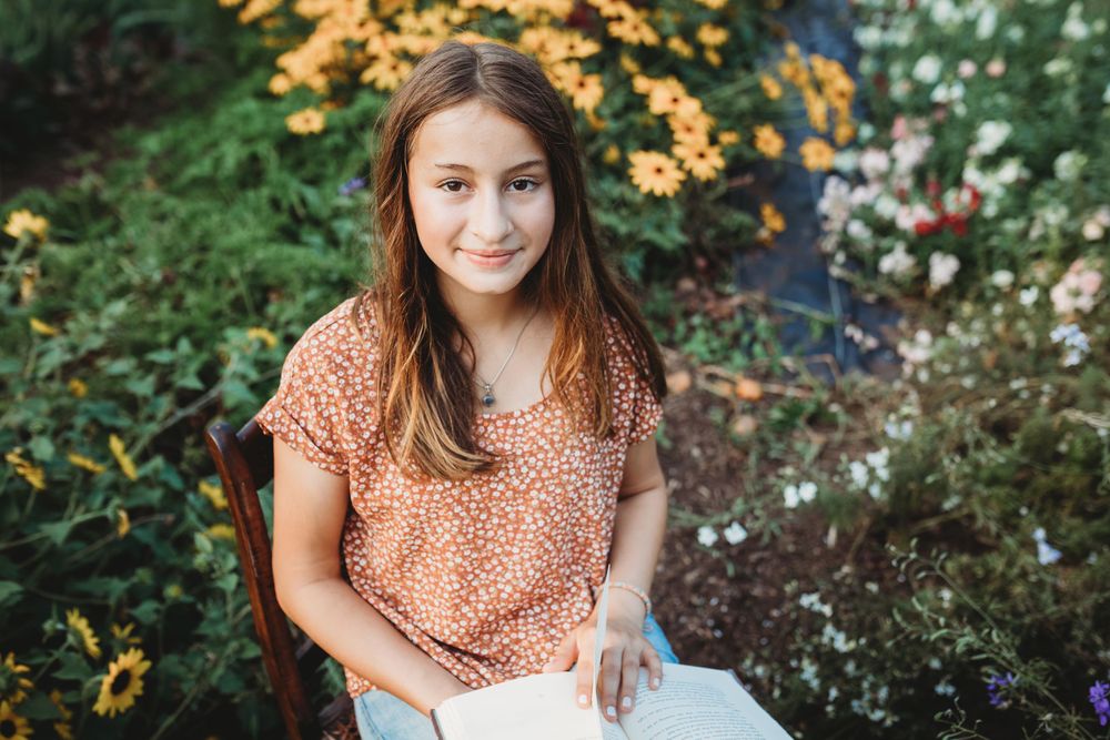 Someone sitting on a wooden chair in a garden with yellow and white flowers.