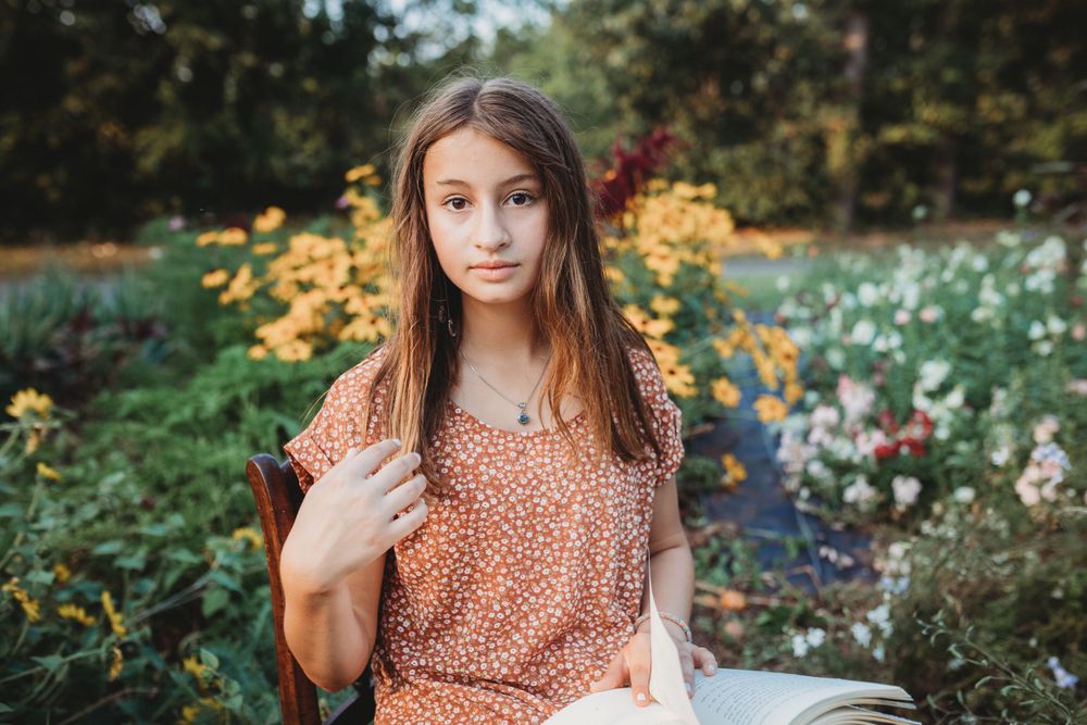 Someone in a peach floral top posing in a garden with yellow flowers.
