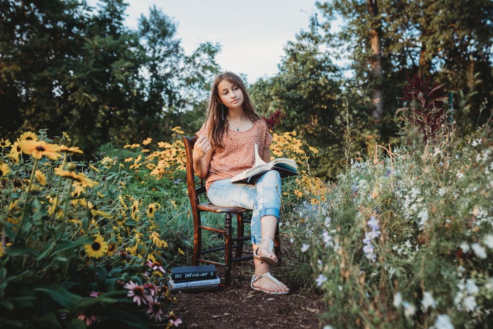 Someone seated on wooden chair surrounded by wildflowers in late summer garden.