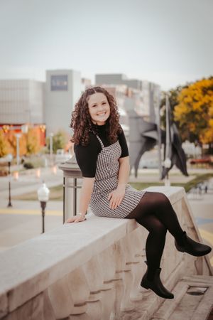 Urban portrait of woman in striped dress sitting on concrete ledge with fall foliage.
