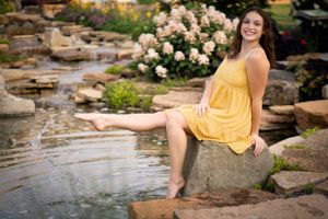 Yellow sundress-clad person sitting by a garden water feature on rocks.