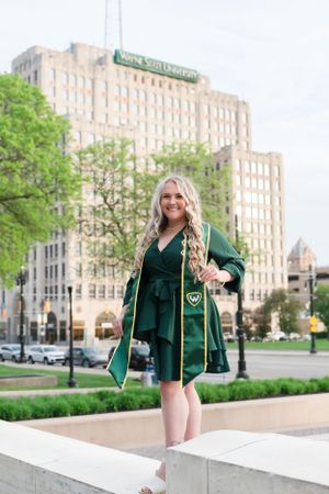 Graduate in emerald green dress posing in front of historic university building.