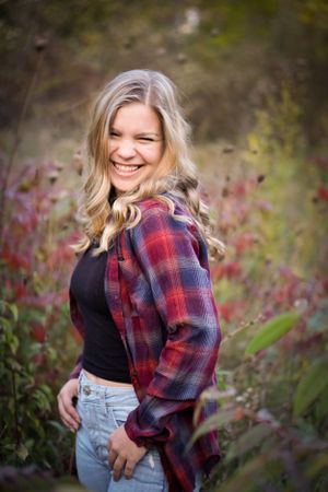 Portrait of a smiling woman wearing a red plaid flannel shirt and black top in an outdoor autumn setting.