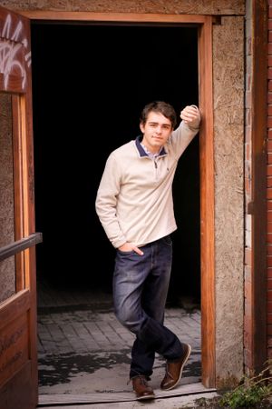 Person in beige sweater leaning in doorway of brick building.