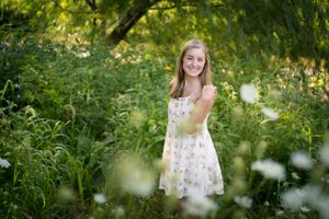 Portrait of young woman in white floral dress standing among wildflowers.