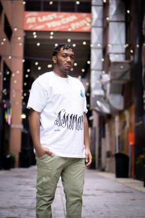 Person in white graphic t-shirt and cargo pants poses on city sidewalk with string lights.
