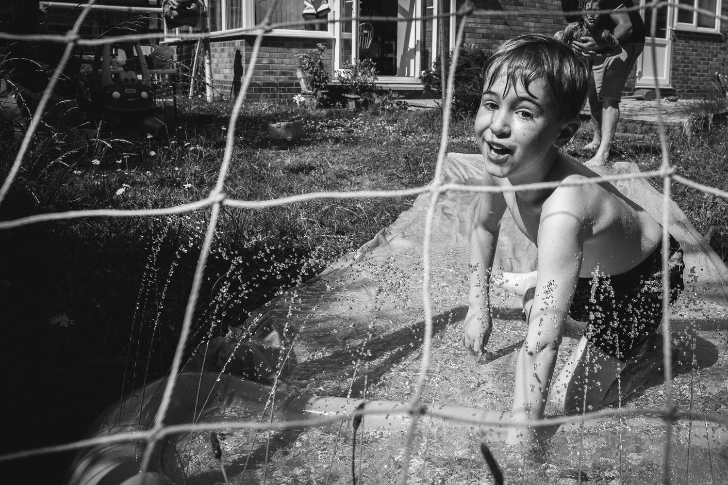 Black and white photo of someone playing in water sprinklers on a summer day.