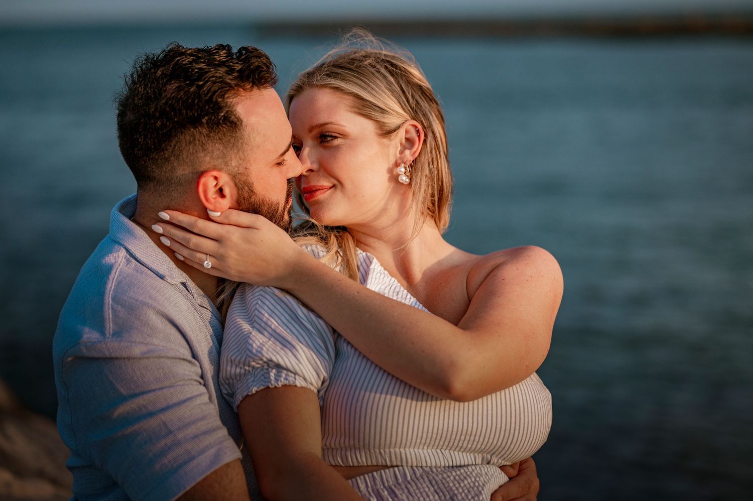 Romantic couple embracing at sunset by the water in warm golden light.