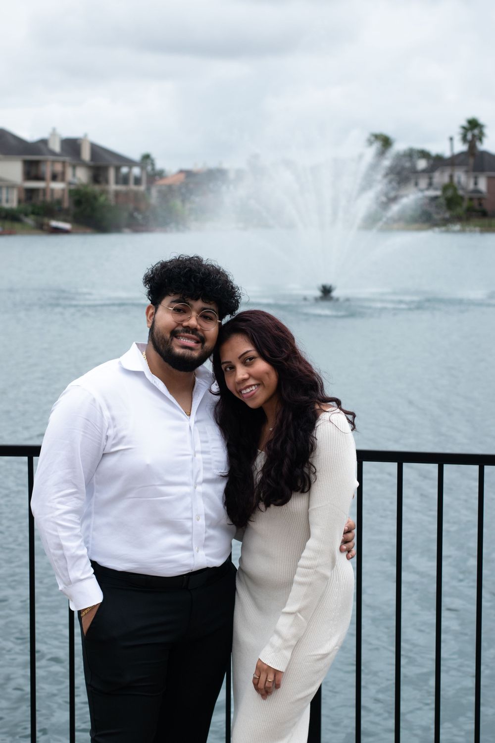 A couple poses together near a waterfront fountain at dusk.