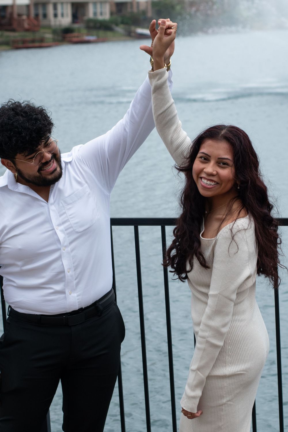 A joyful couple raises their joined hands in celebration by the water.