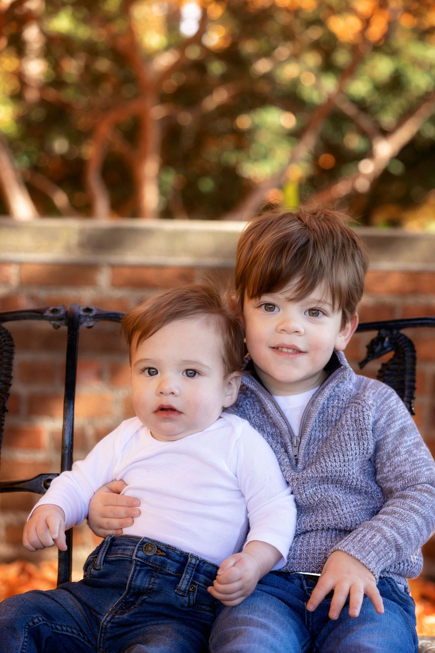 Two young siblings sitting together on iron bench during autumn season.