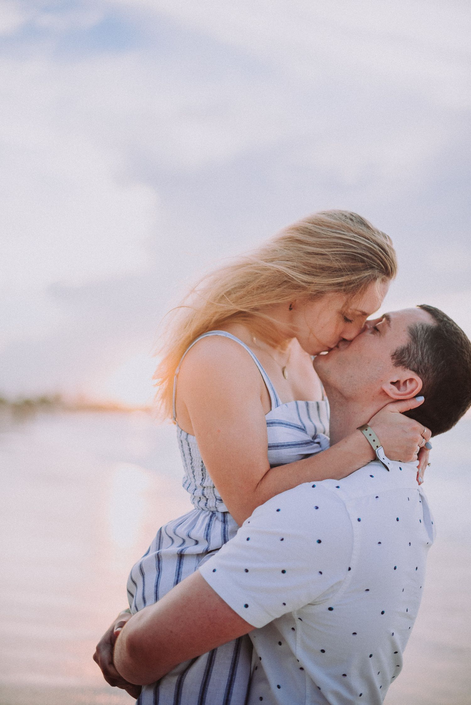 Romantic couple embracing and kissing on beach during golden hour sunset.