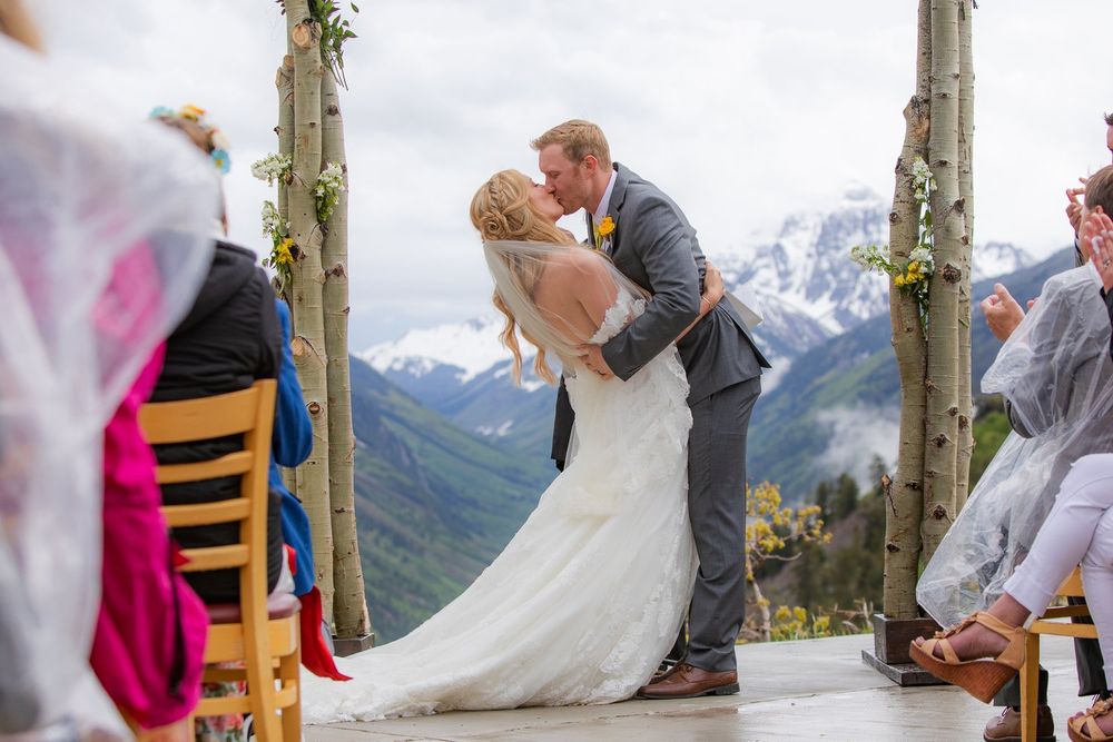 A wedding ceremony with snow-capped mountain peaks in the background as guests watch from wooden chairs.