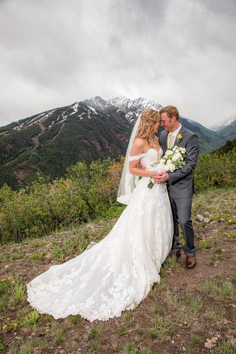 Mountain wedding portrait with dramatic cloudy skies and snow-capped peaks in the background.