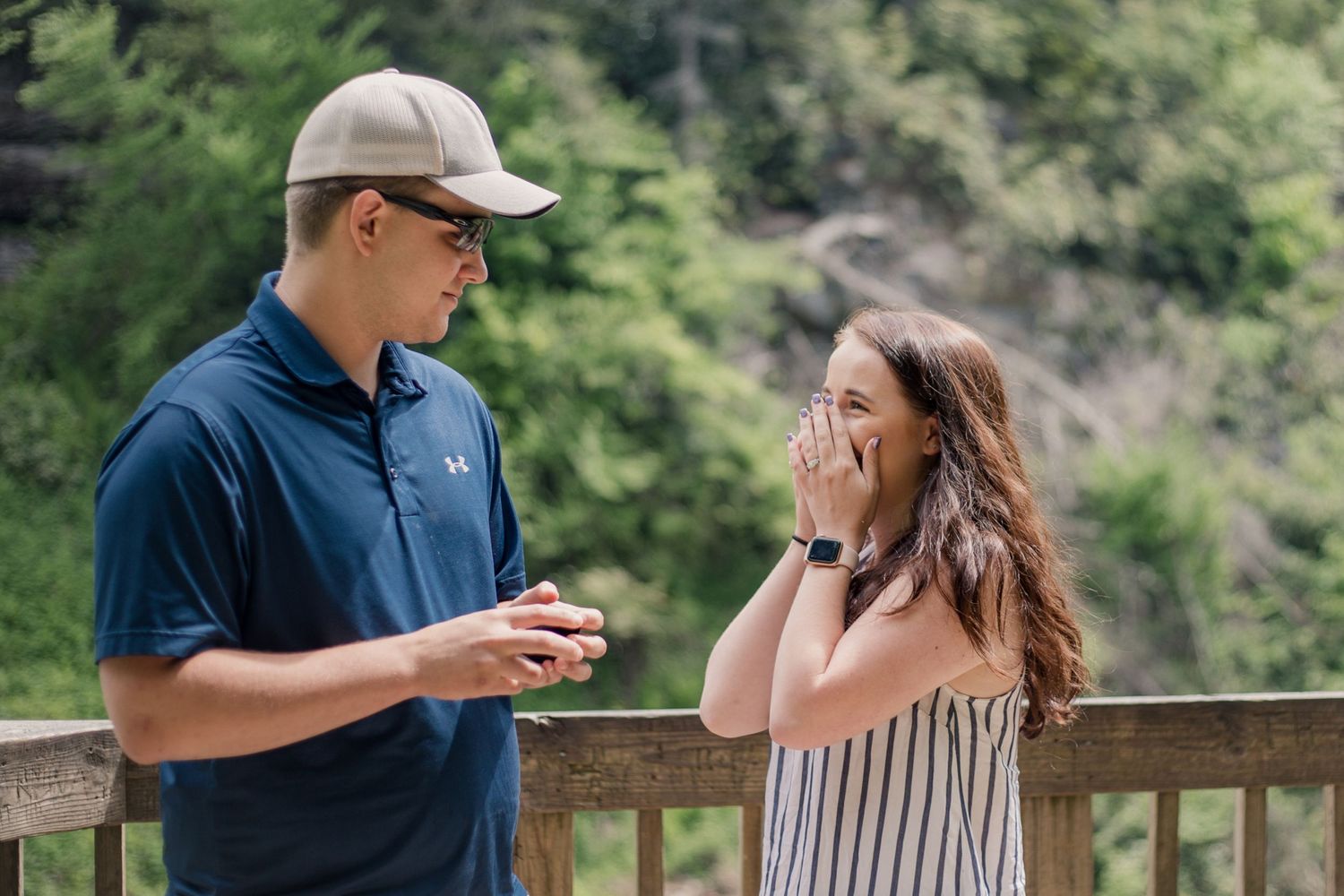 A romantic proposal scene unfolds on a wooden observation deck surrounded by mountain scenery.