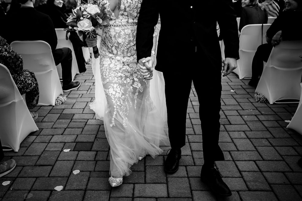 Black and white image of wedding couple walking on brick patio during reception.