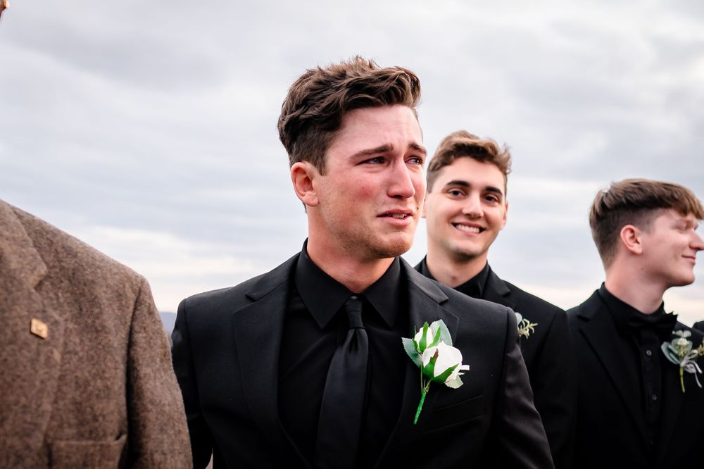 Groomsmen in black suits standing together outdoors.