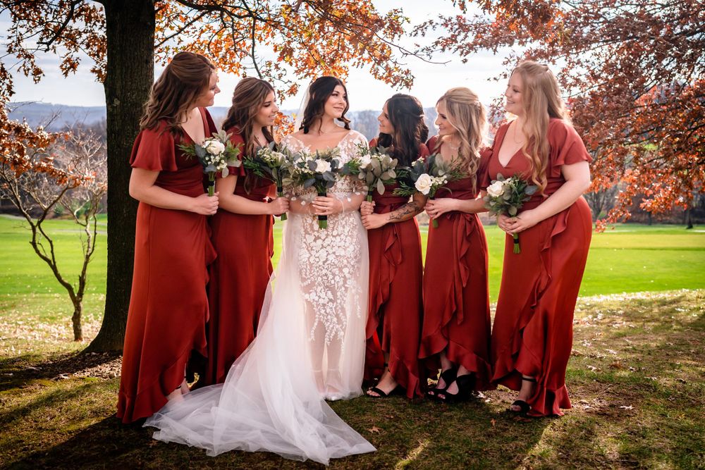 Wedding party poses under autumn trees with red and orange foliage.