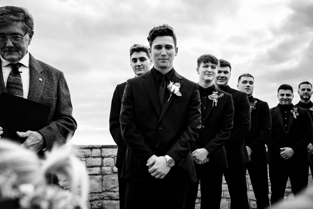 Groomsmen in black suits posing outdoors in black and white photography.