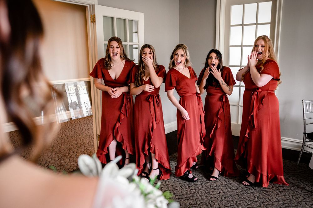 Bridesmaids in matching red dresses gather together in an elegant room.