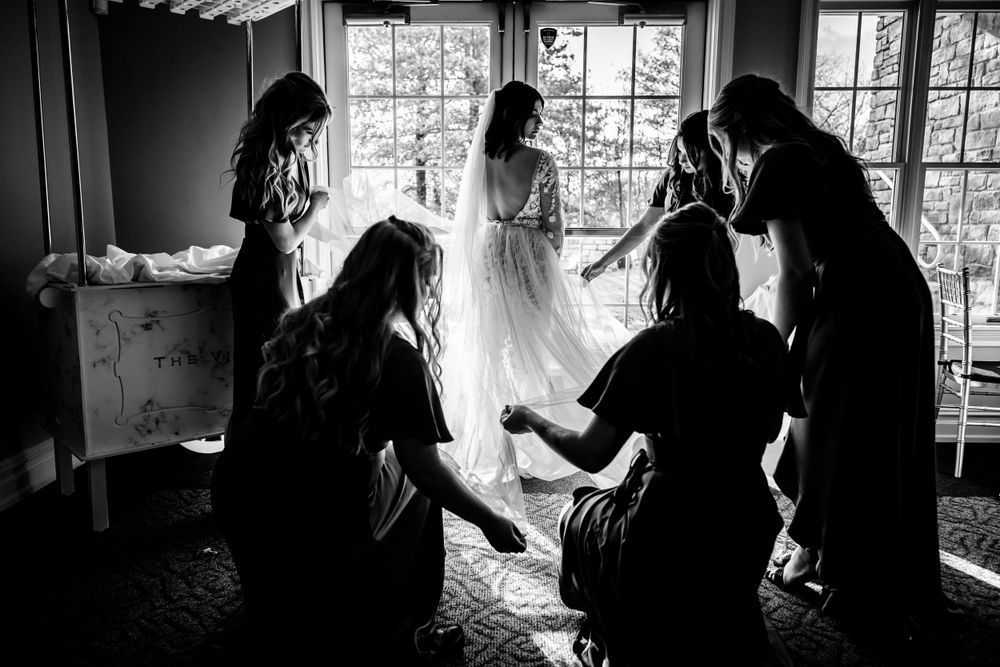 Silhouetted figures prepare by window light in dramatic wedding day scene.