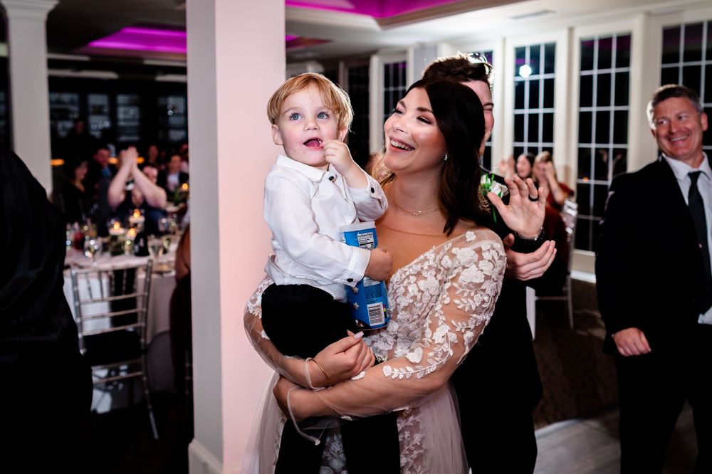 Lively wedding reception celebration with guests dancing under purple ambient lighting.