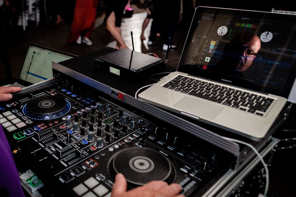 DJ equipment and controllers set up at a party with laptops and mixing boards.
