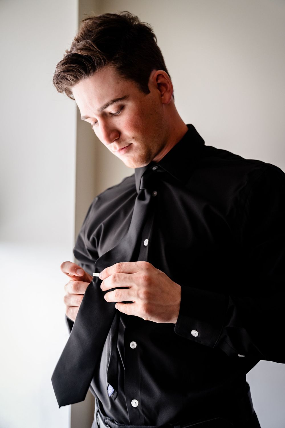 Person in black formal attire adjusting tie in preparation sequence.
