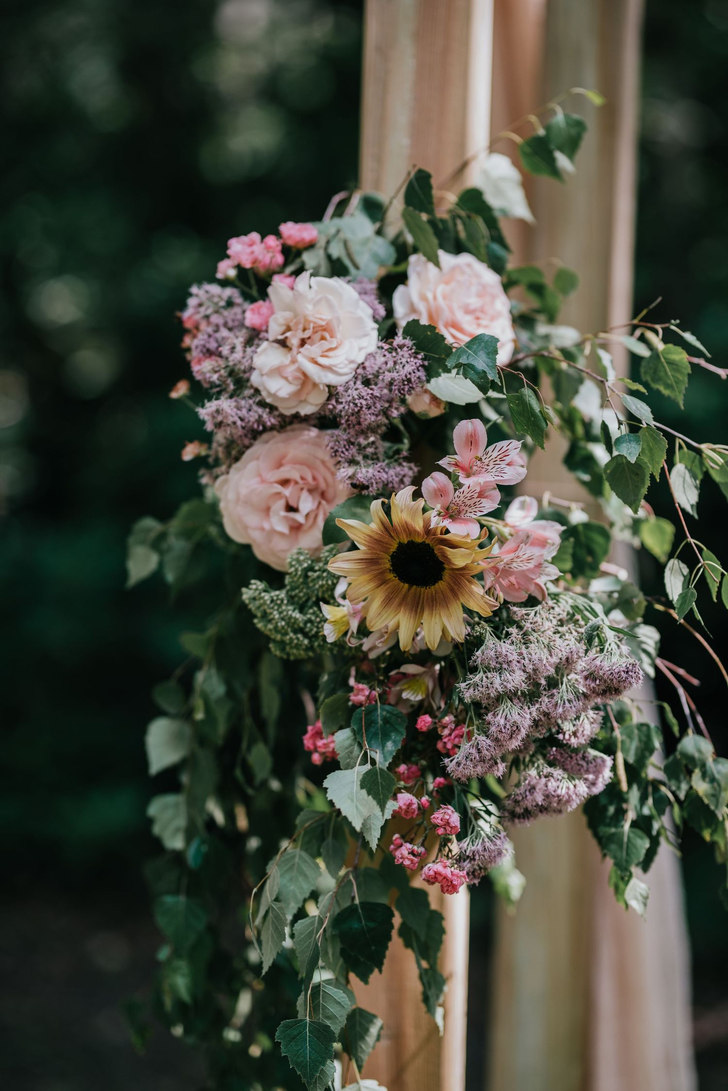 Romantic floral arrangement with roses, sunflower and greenery on a wedding arch.