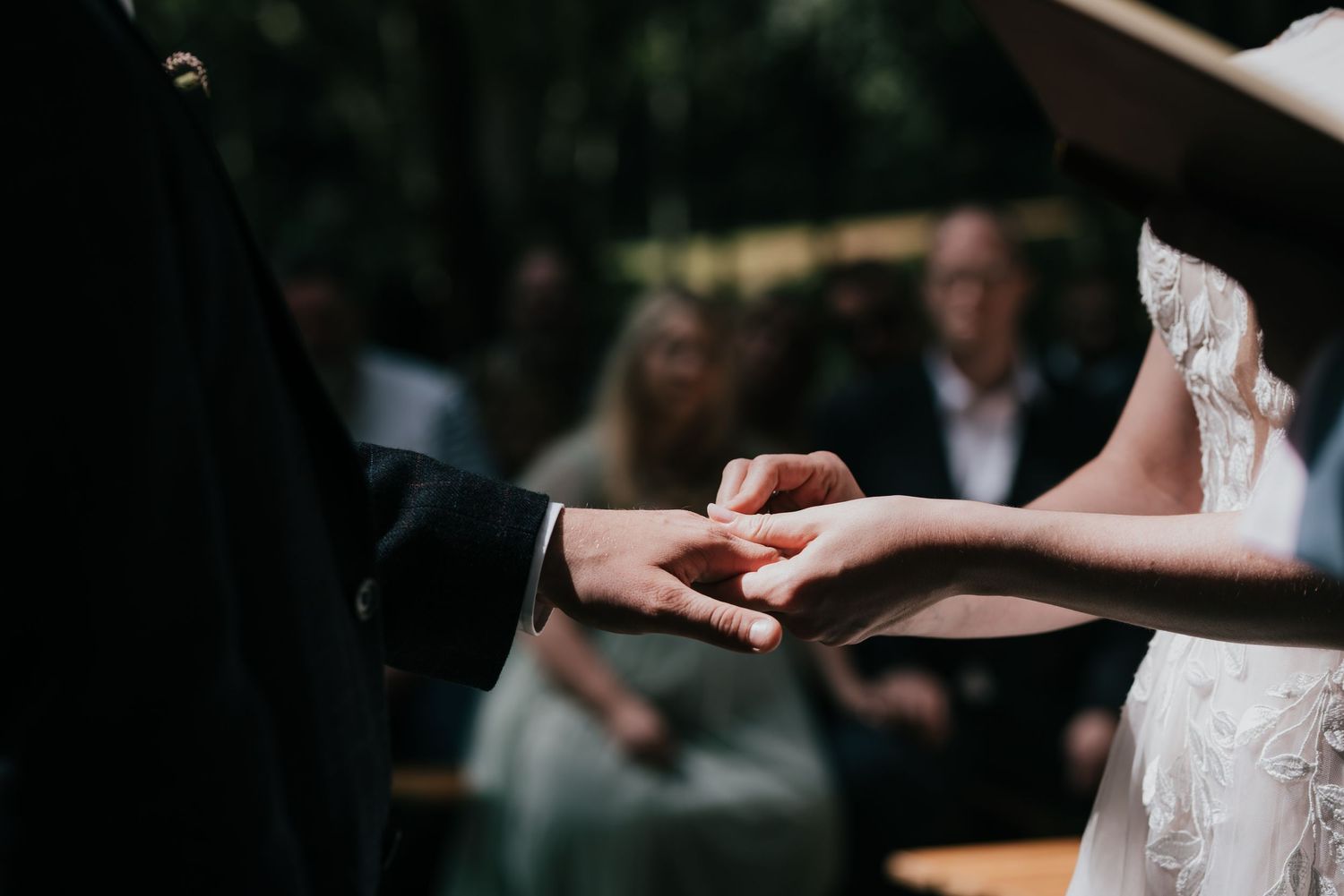 Close-up of hands exchanging rings during outdoor wedding ceremony.