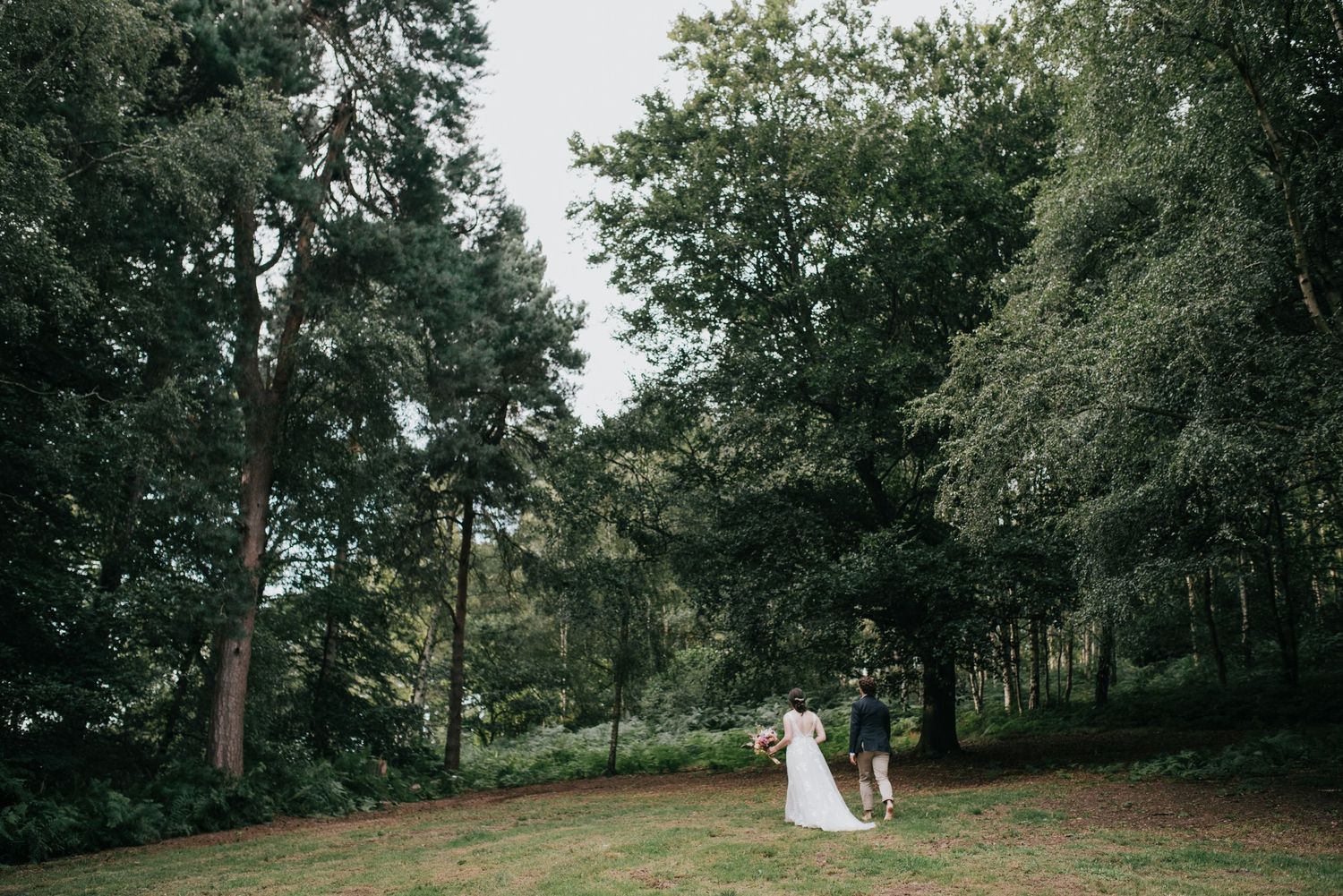 A distant view of a couple walking through a serene wooded area on their wedding day.