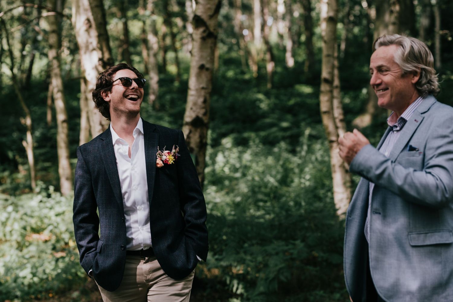 Two people sharing a candid laughing moment in a wooded outdoor setting.