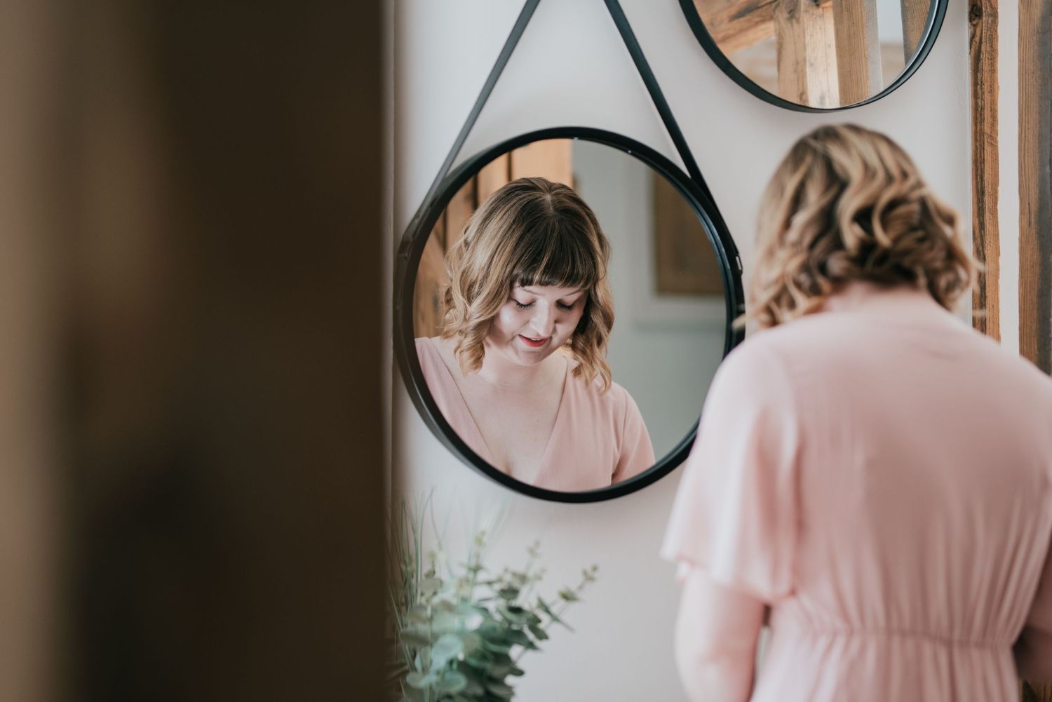 Reflection in a round mirror showing someone wearing a pink dress.