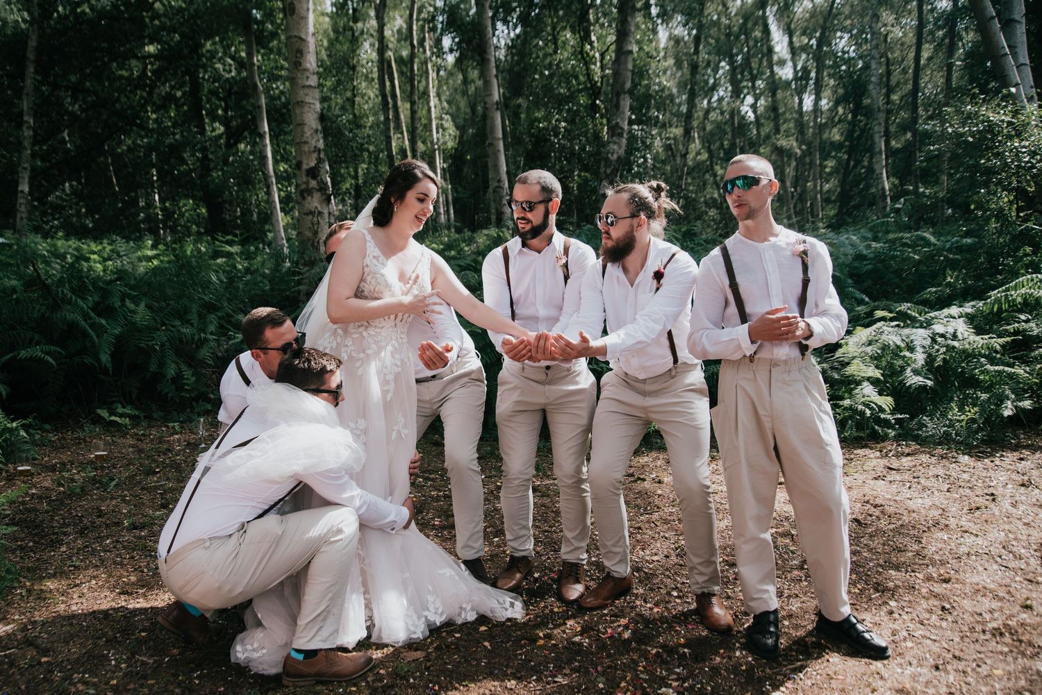 Wedding party in light colored attire sharing laughter on a wooded forest path.