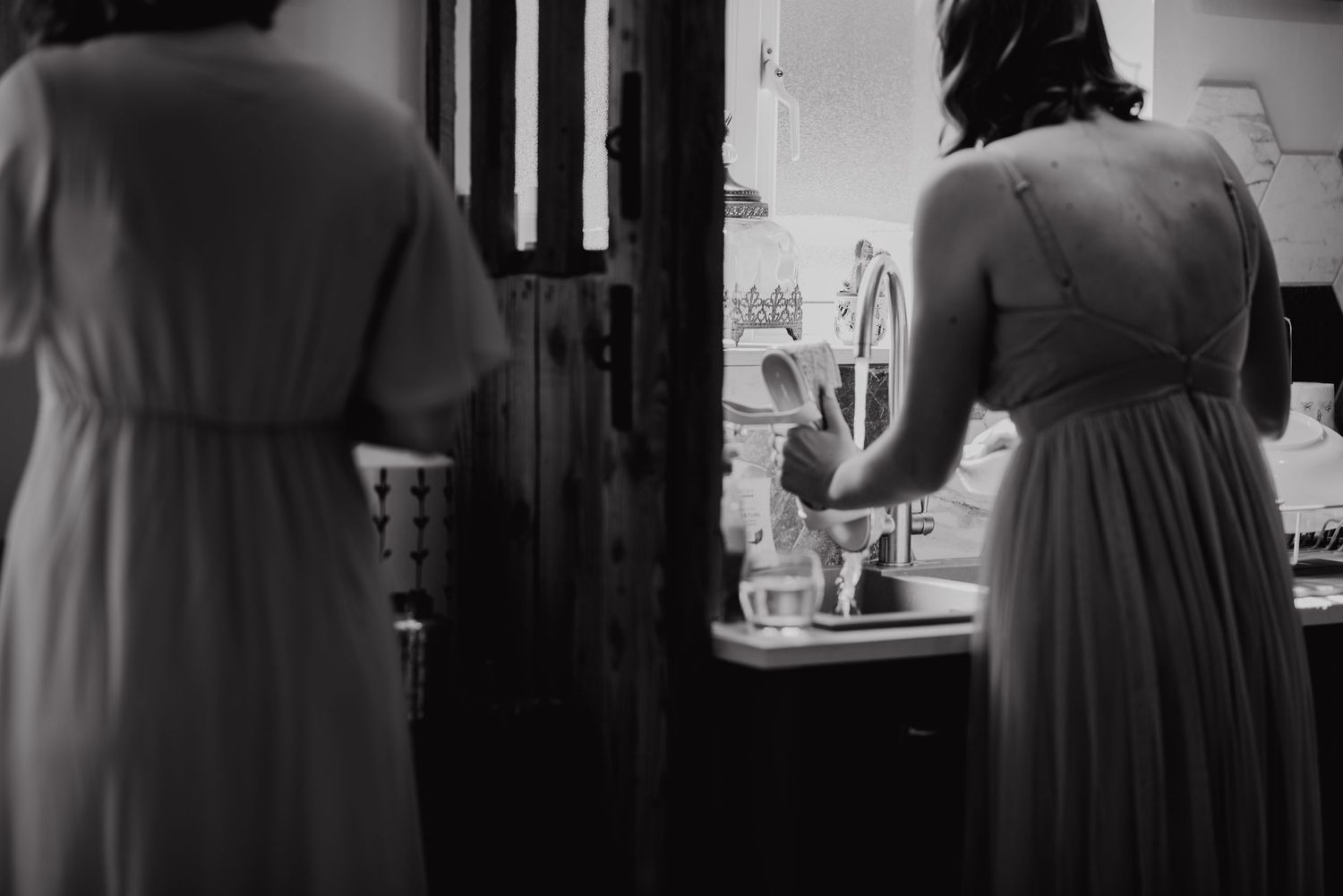 Black and white image of two people in flowing dresses standing at a kitchen sink.