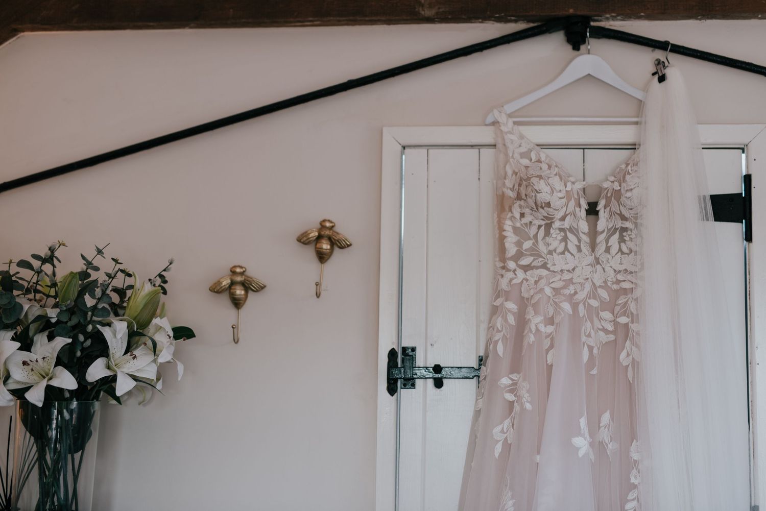 Elegant lace wedding dress hanging on display with floral wall decorations.