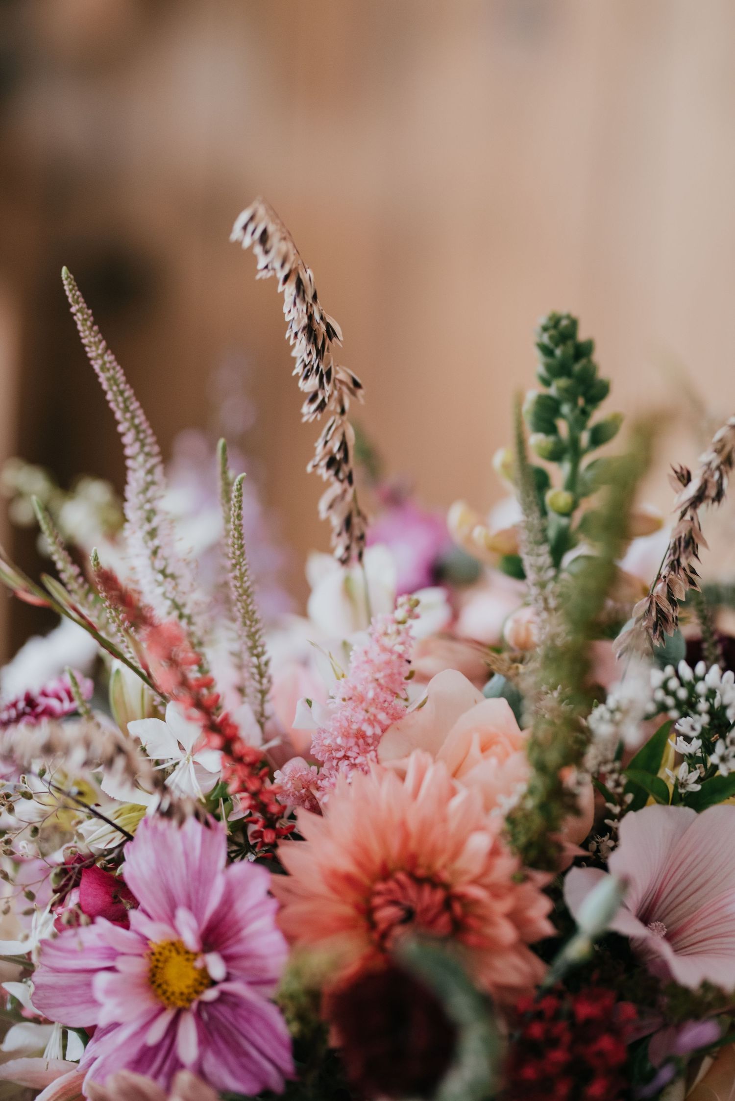 Macro shot of pink, coral and purple wedding flowers with delicate dried grasses and greenery.