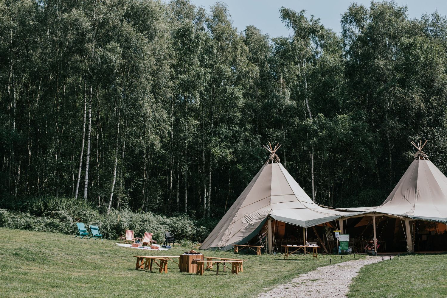 Two large tipi tents set up in a grassy field with forest backdrop.