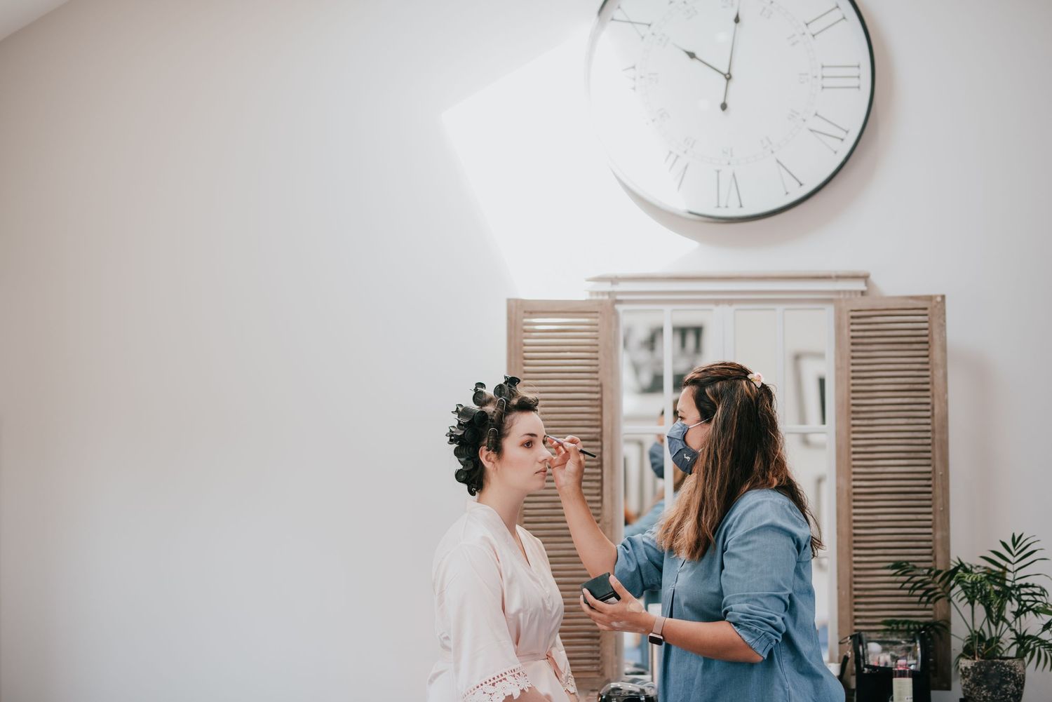 Getting ready scene with makeup application in a bright room with a large wall clock.