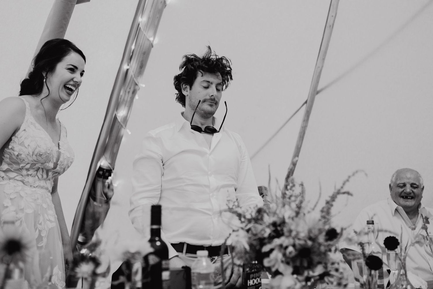 A black and white candid moment showing guests laughing during wedding reception speeches.